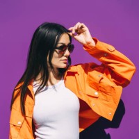 a beautiful young asian woman in sunglasses and a bright orange jacket on a purple background. - fashion stock pictures, royalty-free photos & images