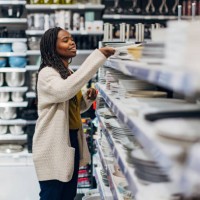 a black woman stands next to a shelf of plates displayed in a department store. she chooses dishes for her new apartment - home decoration stock pictures, royalty-free photos & images