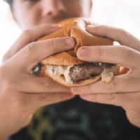 a boy eating a delicious burger in a restaurant - junk food stock pictures, royalty-free photos & images