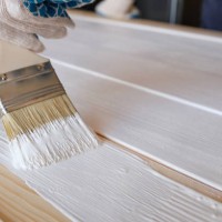 a brush with white paint in the hands of a woman or a man wearing protective gloves. there is a can of paint next to it. painting and repair work. a female artist draws a board and a surface. the concept of repair and constru