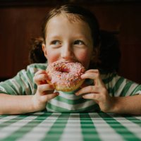 a child smiles as she takes a bite of a pink glazed donut with sprinkles - junk food stock pictures, royalty-free photos & images
