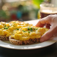 a cropped image of a woman's hand holding a piece of toasted bread with scrambled eggs on top, as she enjoys a healthy breakfast in the morning - food stock pictures, royalty-free photos & images