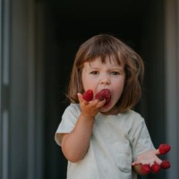 a cute toddler girl with funny facial expression eating raspberry - food stock pictures, royalty-free photos & images