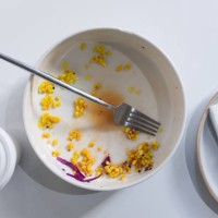 a dirty empty plate and fork on a wooden kitchen or dining table. cutlery is used, symbolizing the end of lunch or dinner. a portion of food eaten, overeating. next to it is a disposable paper coffee mug. completion of lunch 