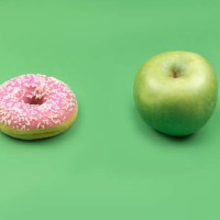 a donut and an apple on green background. - junk food stock pictures, royalty-free photos & images