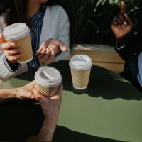 a group of colleagues sit at a table outdoors and enjoy some takeaway coffees - coffee stockfoto's en -beelden