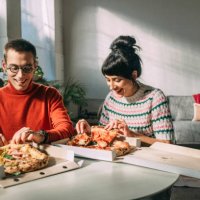 a handsome man and his girlfriend smiling while taking a slice of pizza - junk food stock pictures, royalty-free photos & images