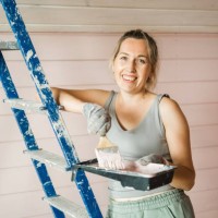 a happy caucasian woman paints the inner wall of a new house with a brush, looks at the camera and smiles. - home decoration stock pictures, royalty-free photos & images
