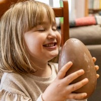 a happy little girl with her eyes closed holding a chocolate easter egg at home - junk food stock pictures, royalty-free photos & images