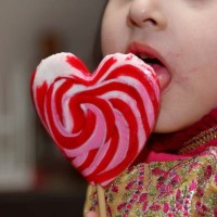 a little cute girl eating and licking heart shape lollipop. - junk food stock pictures, royalty-free photos & images