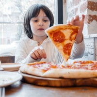 a little girl eats pizza in a pizzeria. the cute girl eats pizza with an appetite. - junk food stock pictures, royalty-free photos & images