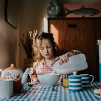 a little girl pours milk on her breakfast cereal in a morning dining table scene - junk food stock pictures, royalty-free photos & images