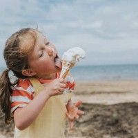 a little girl stands on a beach and eats a melting ice-cream - food fotografías e imágenes de stock
