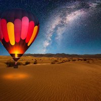a majestic hot air balloon soars under the stars of the milky way, over the desert - mesquite dunes of death valley national park. moonlight provides luminosity showing the patterns and shapes of the desert landscape. - trave