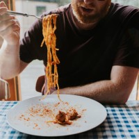 a man eats a plate of spaghetti bolognese with meatballs at a dining table - food stock pictures, royalty-free photos & images