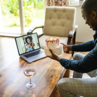a man is showing his birthday cake to a friend via a video call on his laptop - junk food stock pictures, royalty-free photos & images