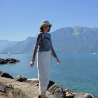 a person stands on a rocky shoreline with a large body of water and mountains in the background, wearing a hat, striped top, and white pants - fashion stock pictures, royalty-free photos & images