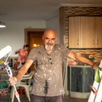 a senior wall painter poses in portrait with tools in hand smiling and looking at camera, full of paint with a roller - home decoration stock pictures, royalty-free photos & images