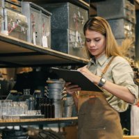a small business warehouse worker owner wearing apron checking inventory count stocktaking product on shelf warehouse storage room - garden decoration stock pictures, royalty-free photos & images