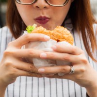 a southeast asian woman is eating hamburger outdoors - junk food stock pictures, royalty-free photos & images