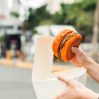 a southeast asian woman is holding a hamburger with paper container and food truck background - junk food stock pictures, royalty-free photos & images