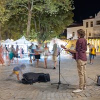 a street musician plays and sings to passers-by in a square of a small resort town. - concert stock pictures, royalty-free photos & images