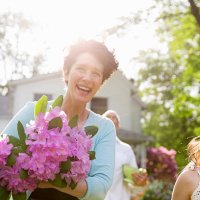 a summer family gathering at a farm. a woman carrying a large bunch of rhododendron flowers, smiling broadly. - garden decoration stock pictures, royalty-free photos & images