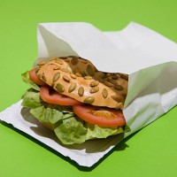 a sunflower seed bagel sandwich with tomato and lettuce in a paper bag - junk food stock pictures, royalty-free photos & images