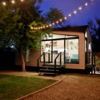 a tiny house with large glass windows, sits in the backyard at night, surrounded by trees and party lights. - garden decoration stock pictures, royalty-free photos & images