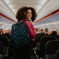 a woman boards a commercial aircraft with hand luggage. she glances over her shoulder and smiles at the camera. - travel stock pictures, royalty-free photos & images