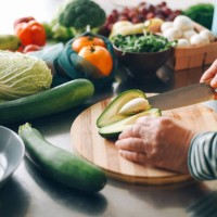 a woman cuts a ripe avocado and takes out a stone from it on a wooden plank. fresh vegetables. salad preparation. diet food. ecological products. - food stock pictures, royalty-free photos & images