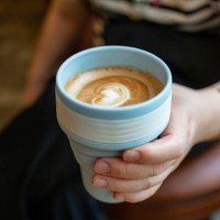 a woman holding a cup of coffee in a reusable mug. - junk food stock pictures, royalty-free photos & images