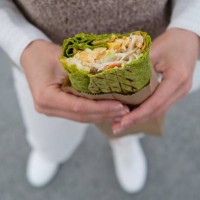 a woman or a girl, a high school student, eats vegetarian or vegan vegetable shawarma on the street. the concept of fast food, takeaway food. lush, burrito, roll in the hands of a woman. junk food, snacks. sustainable develop