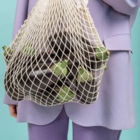 a woman's hand holds a string bag with eggplant on a colored background - fashion stock pictures, royalty-free photos & images