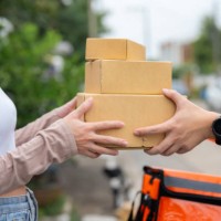 a woman waiting at the door is given food by a smiling delivery man. - junk food stock pictures, royalty-free photos & images