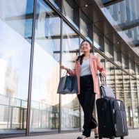 a young beautiful asian business woman with shopping bags in hand while pulling wheeled suitcases at airport terminal - travel stock pictures, royalty-free photos & images