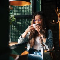 a young beautiful girl is sitting in a cafe by the window and enjoying her coffee. - coffee stock pictures, royalty-free photos & images