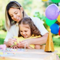a young cheerful mom is having fun with her child, teaching the baby to paint her nails on her birthday - garden decoration stock pictures, royalty-free photos & images