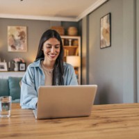 a young cheerful woman sitting at the table in the living room at home and using a laptop. - home decoration photos et images de collection