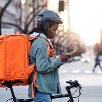 a young delivery woman on her bicycle looking on her smartphone for the route of her delivery - food stock pictures, royalty-free photos & images