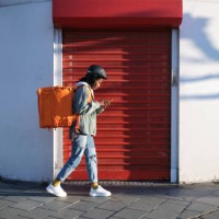 a young delivery woman with her backpack using her phone and walking in search of the delivery place - food stock pictures, royalty-free photos & images