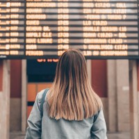 a young woman at a railway station or at the airport looks at the smartphone screen against the background of the arrival and departure board - travel photos et images de collection