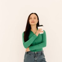 a young woman in a green sweatshirt holds a glass of coffee and smiles at the camera while standing against a white isolated background. space for the text. a place for advertising. copy space - junk food stock pictures, roya