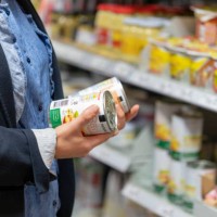 a young woman reads and compares the labels of two cans - junk food stock pictures, royalty-free photos & images
