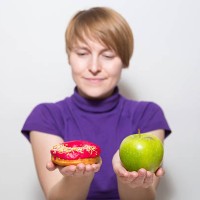 a young woman struggling to choose between an apple and a donut - junk food stock pictures, royalty-free photos & images