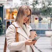 a young woman talking on her smartphone and drinking take-out coffee outdoor - junk food stock pictures, royalty-free photos & images