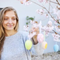 a young woman with blond long hair hangs easter eggs on her cherry tree - garden decoration stock pictures, royalty-free photos & images