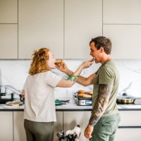adorable couple enjoys cooking together in their well-lit, modern kitchen, playfully sharing bites of food. - food stock pictures, royalty-free photos & images