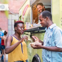 african-american couple enjoying their lunch from food truck in city street. - junk food stock pictures, royalty-free photos & images
