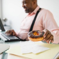 african american businessman eating donut at desk - junk food stock pictures, royalty-free photos & images